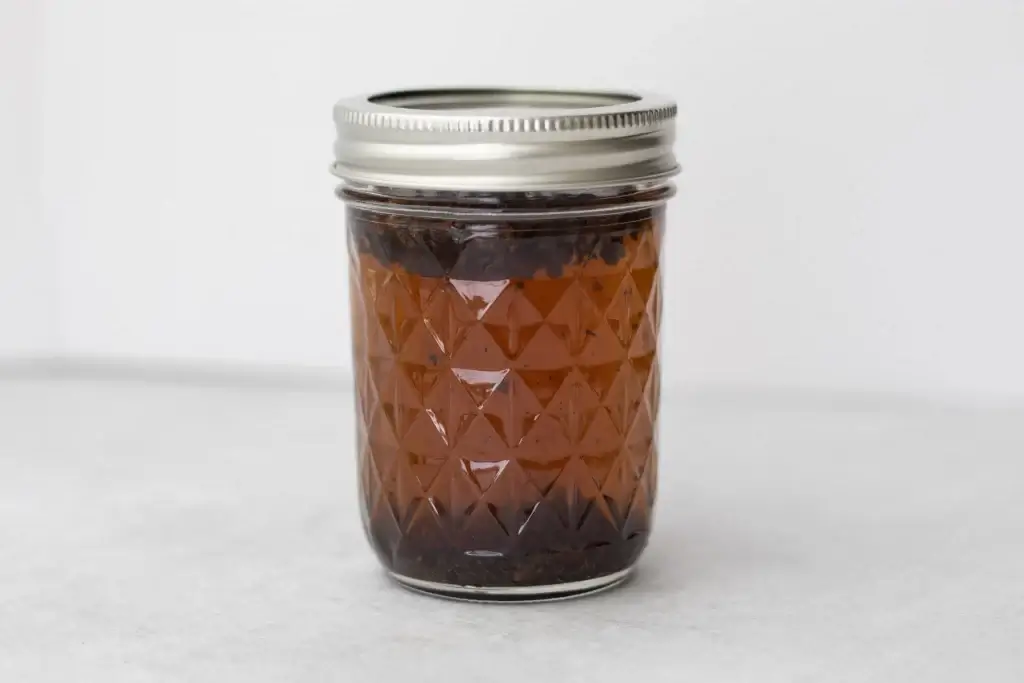 Mason jar filled with allspice berries steeping in brandy