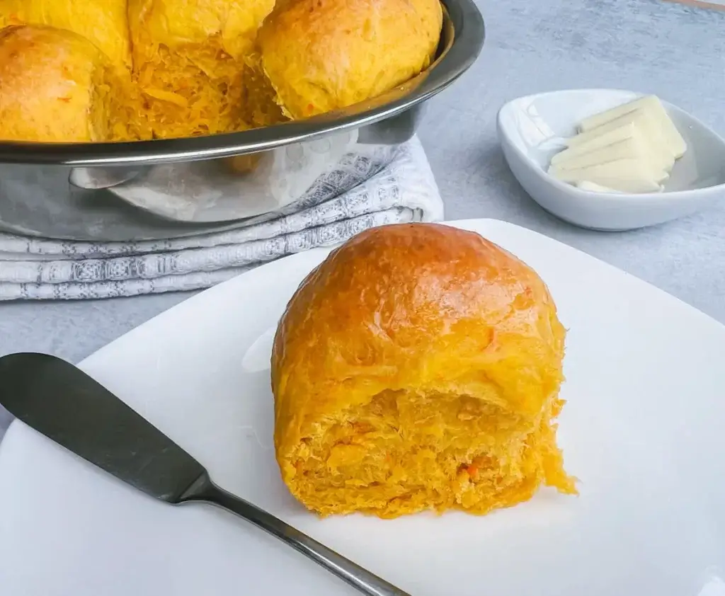 fresh baked sweet potato roll on a white plate about to be buttered