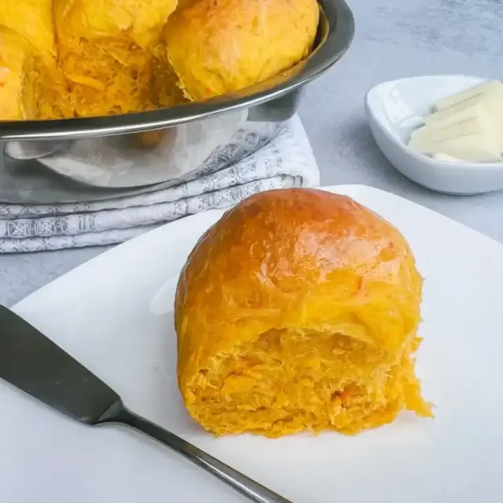 fresh baked sweet potato roll on a white plate about to be buttered