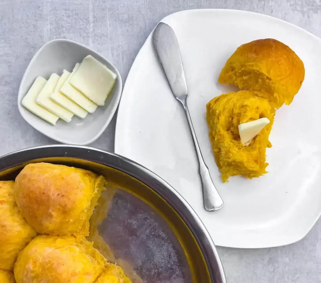 a fresh baked sweet potato roll sliced open on a white plate with a pat of butter