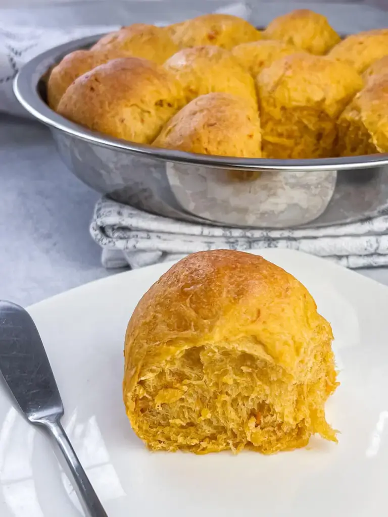 a fresh baked sweet potato roll sliced open on a white plate with a pat of butter